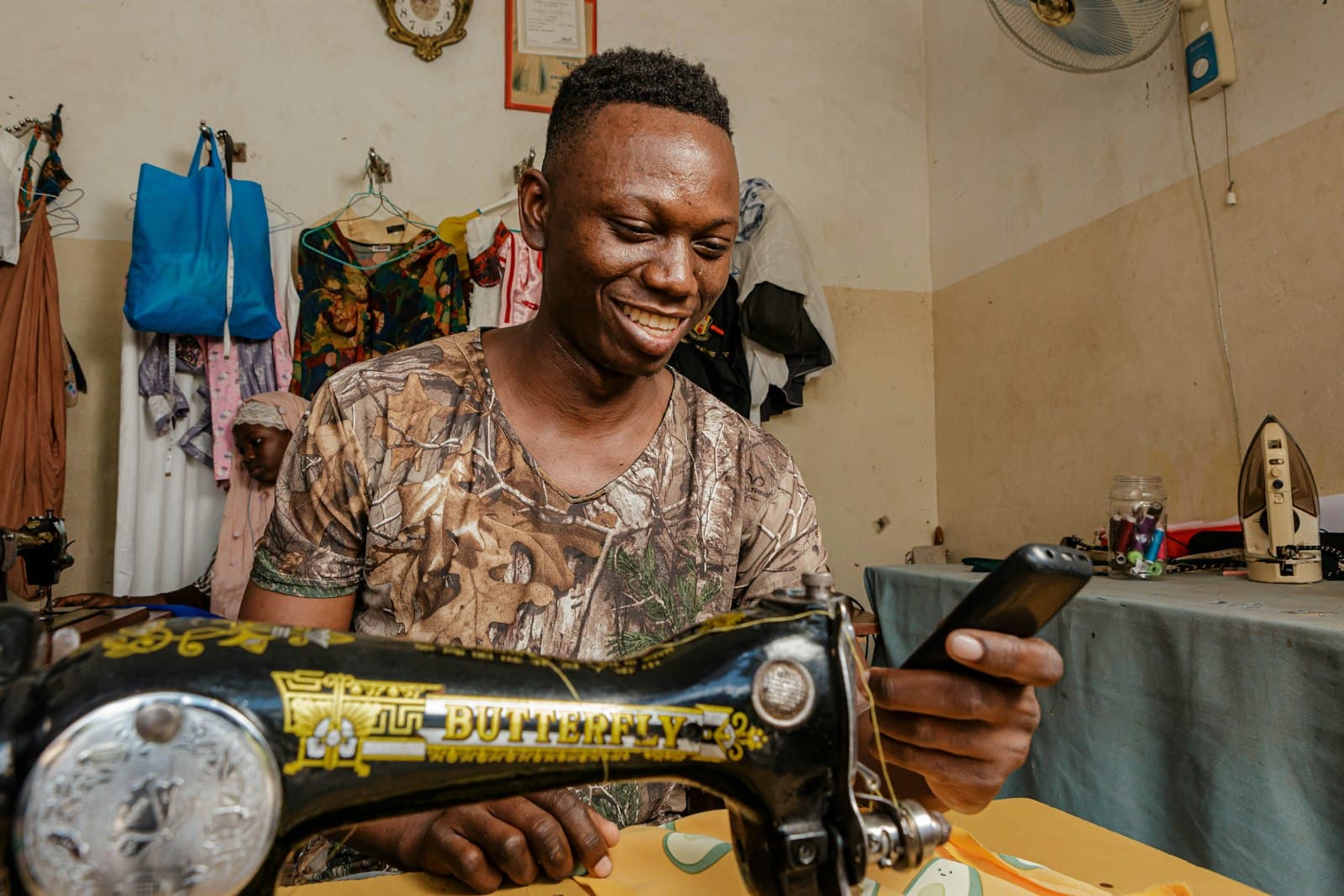 Couturier dans son atelier, téléphone à la main devant sa machine à coudre